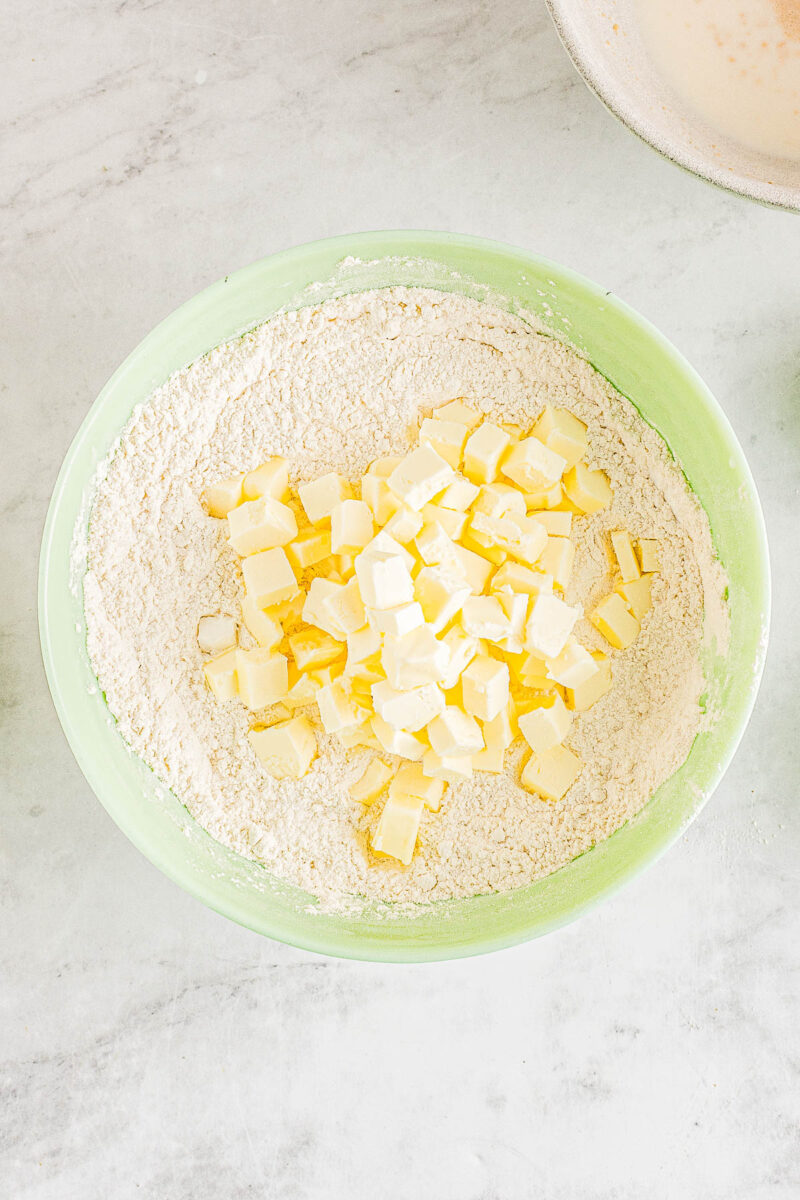 Butter cubes being added to a bowl of dry ingredients for angel biscuits.