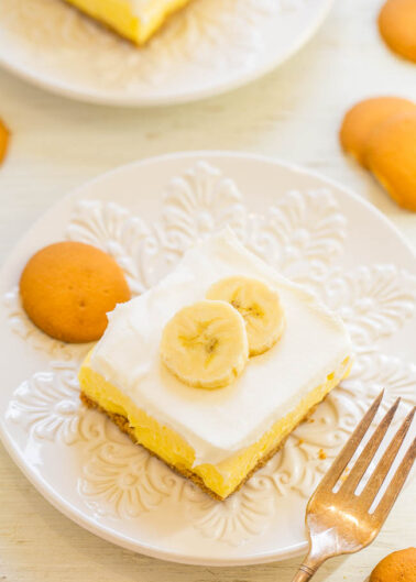 A slice of banana pudding cake on a decorative plate with a fork on the side and whole vanilla wafers surrounding it.
