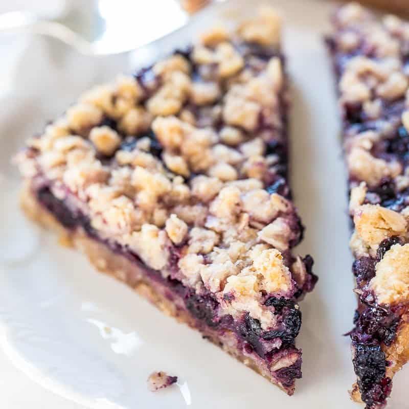 A close-up of a blueberry crumble pie slice on a white plate.