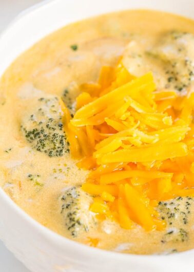 A bowl of broccoli cheddar soup topped with shredded cheese.