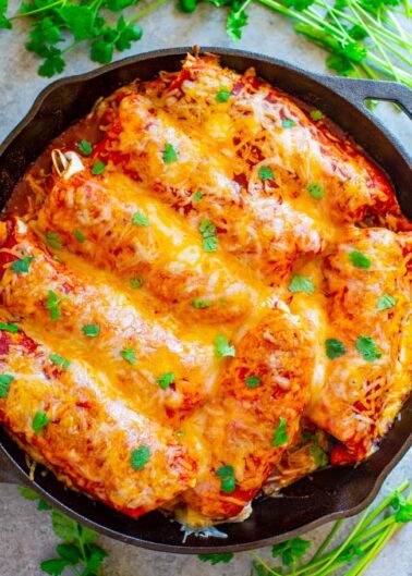 A skillet filled with baked enchiladas topped with melted cheese and garnished with fresh herbs.