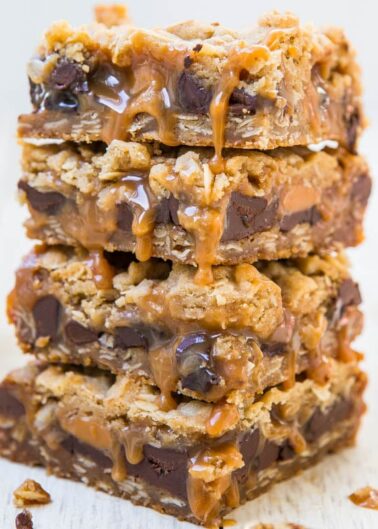 Stack of gooey caramel and chocolate chip blondies on a white surface.