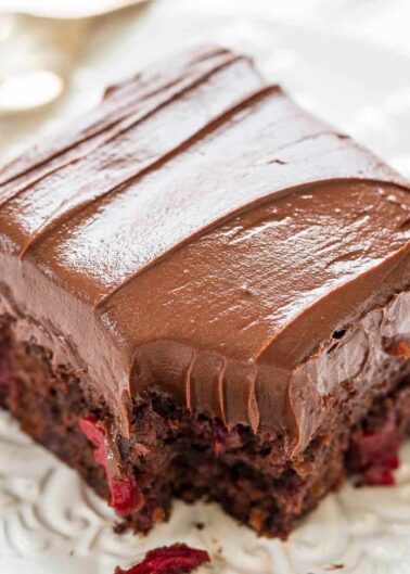A chocolate frosted brownie with red berry pieces on a white plate.