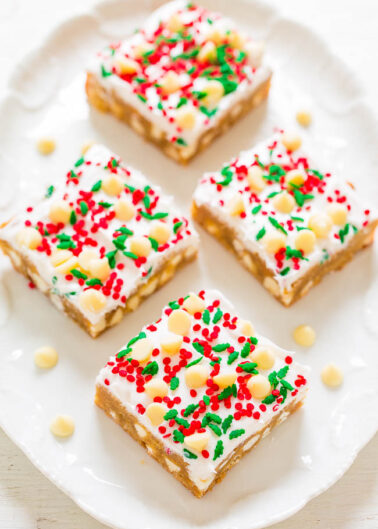 Four frosted holiday sugar cookies with red, green, and white sprinkles on a white plate.