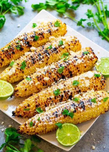 Grilled corn on the cob garnished with herbs and spices on a serving plate.