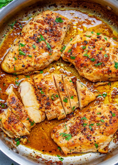 Pan-seared chicken breasts with a golden-brown crust and herb garnishing, served in a savory sauce.