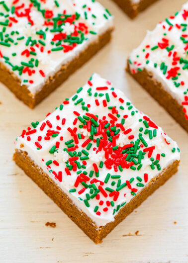 A piece of festive gingerbread cake topped with white icing and red and green sprinkles.