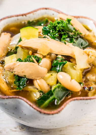 A bowl of hearty vegetable and bean soup on a wooden surface.