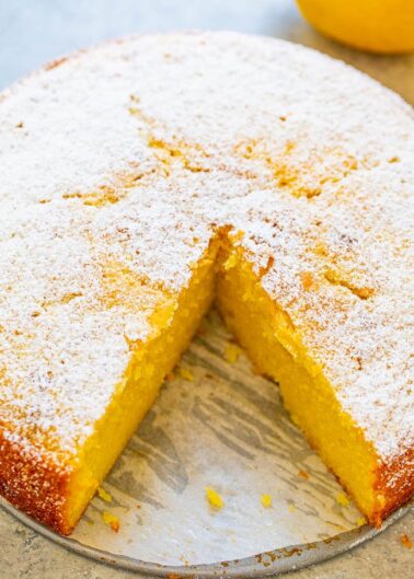 A freshly baked lemon cake with a slice removed, dusted with powdered sugar.