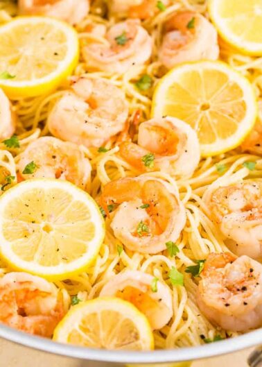 A pan of lemon garlic shrimp pasta garnished with parsley and lemon slices.