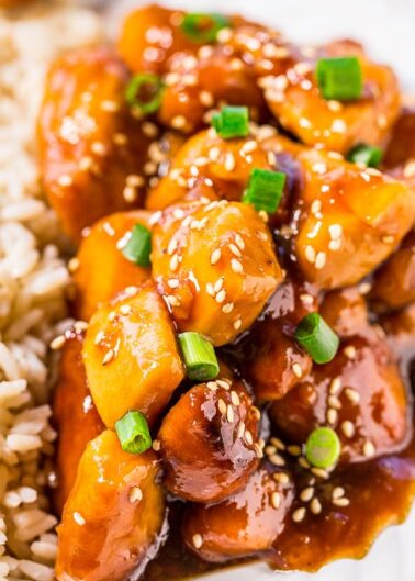 Plate of sesame chicken with rice garnished with green onions.