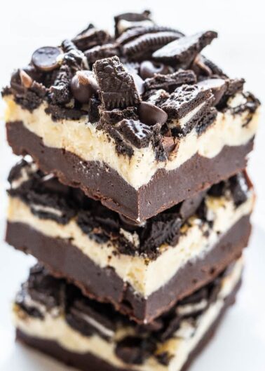 Two stacked oreo cheesecake bars with chocolate topping and cookie pieces.