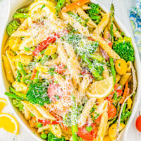 A serving dish full of pasta primavera topped with parmesan cheese.