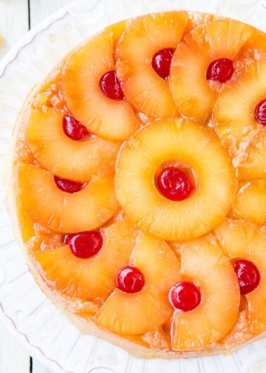 A pineapple upside-down cake with cherries on a white plate.