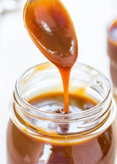 A spoon dripping caramel sauce into a jar.