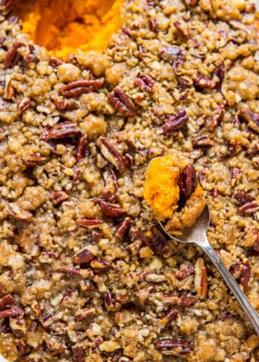 A sweet potato casserole topped with pecans and a spoonful being scooped out.