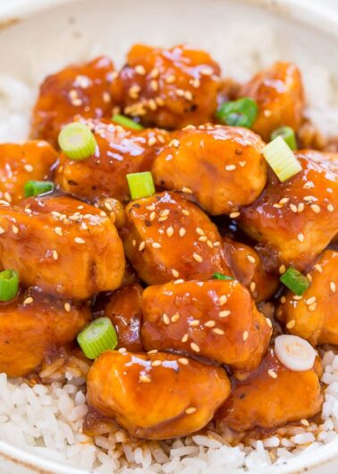 A bowl of sesame chicken served over white rice, garnished with scallions.
