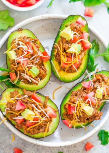 Stuffed avocados with taco filling and shredded cheese, garnished with diced tomatoes.