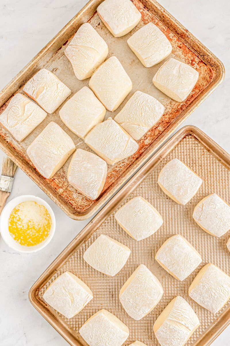 Proofed Texas Roadhouse dinner rolls on two baking sheets.