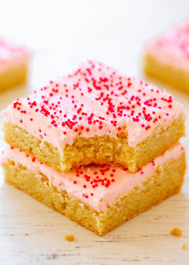 Three stacked sugar cookie bars with pink frosting and red sprinkles on a white surface.