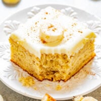 A slice of banana cake with cream cheese frosting with a bite missing.