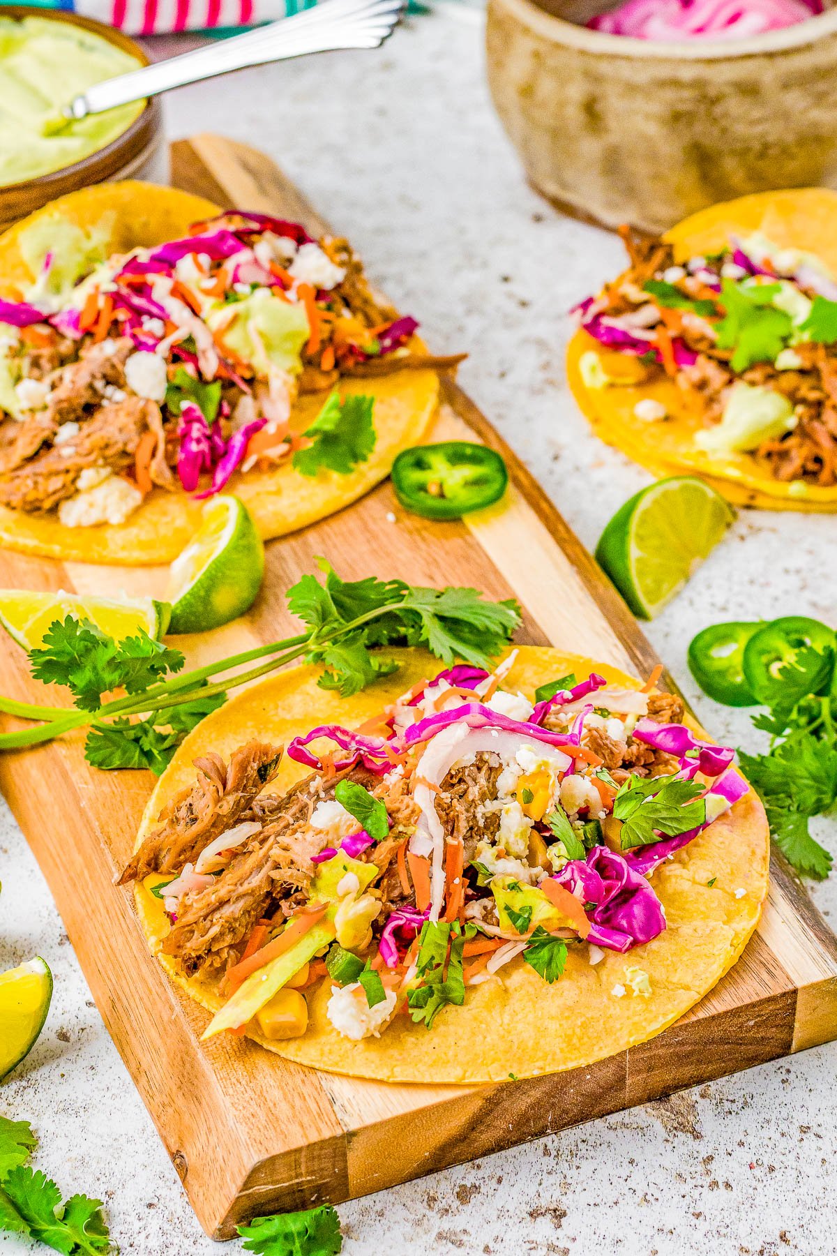 Pulled Pork Tacos - The BEST pulled pork tacos made with slow cooker pulled pork, nestled in tortillas, and then topped in abundance with Cilantro Lime Slaw, Pickled Red Onions, and Avocado Crema! Learn how to make these Mexican-inspired classic recipes at home! Easy enough for weeknights but also great for events, game day parties, get-togethers like Cinco de Mayo fiestas or graduation parties! 