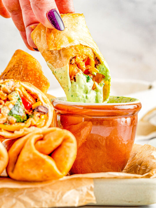 Southwestern Egg Rolls - Juicy chicken, melted Pepper Jack cheese, black beans, bell peppers, and corn seasoned with southwest-inspired seasonings and fried to crispy PERFECTION! You can fry, air fry, or bake these EASY egg rolls which are a Chili's Restaurant copycat. The quick creamy mashed avocado ranch dipping sauce is the perfect final touch!