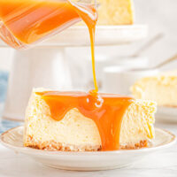 Caramel sauce being drizzled over a slice of New York cheesecake.