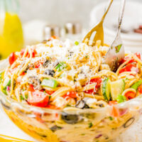 Spaghetti Pasta Salad in a bowl topped with Parmesan, serving tongs sticking out.