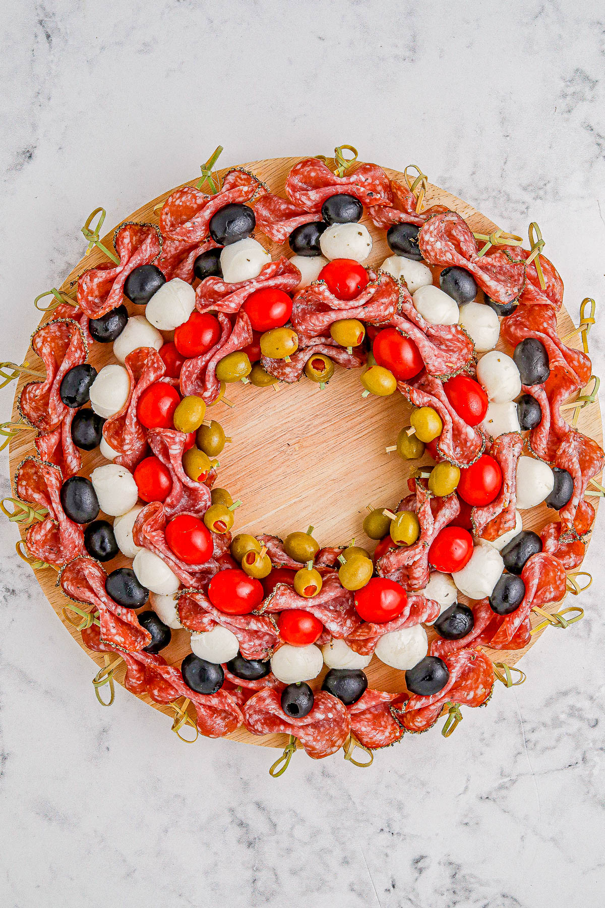 Holiday Antipasto Wreath - A fun and festive Christmas or New Year's Eve appetizer recipe idea that's so FAST and EASY to make! Skewered salami, mozzarella, tomatoes, olives, fresh herbs, and more come together to form the wreath. Mix-and-match the ingredients based on your favorites. You can prep it ahead of your party or event and when your guests see this, I guarantee everyone's eyes will light up!