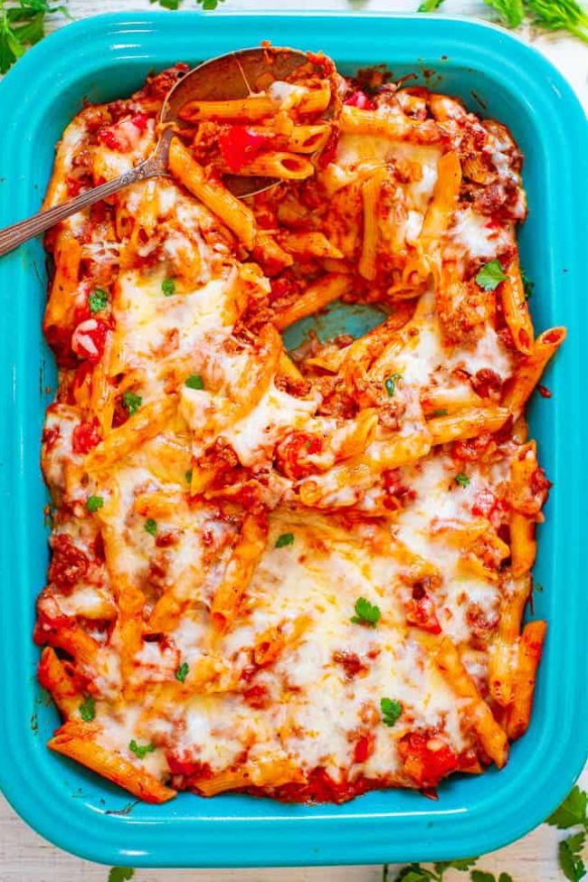A dish of baked ziti with melted cheese and herbs in a blue baking dish.