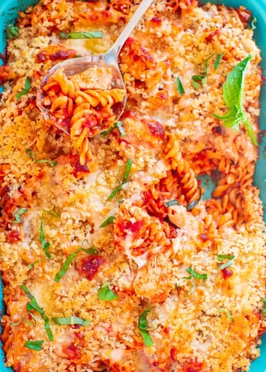 A baked pasta dish with a golden breadcrumb topping, garnished with basil in a blue baking dish.