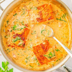 Creamy Garlic Butter Tuscan Salmon in a skillet with a spoon sticking out.