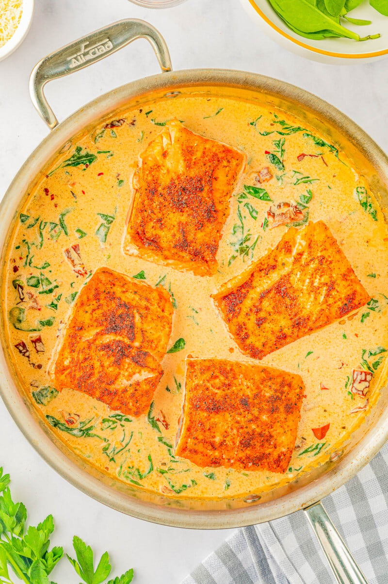 Creamy Garlic Butter Tuscan Salmon - An EASY one-skillet salmon recipe for the most tender and juicy salmon that's bathed in a rich and creamy garlic butter sauce! Parmesan cheese, sun dried tomatoes, and baby spinach add extra flavor and texture to this 30-minute recipe that everyone LOVES! Learn how to make restaurant-worthy salmon that's fast enough for a weeknight dinner but elevated enough to serve to company!