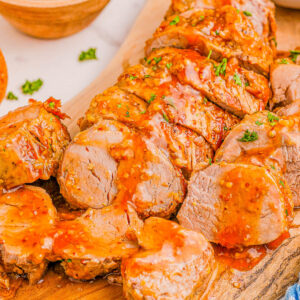 Sliced roasted pork tenderloin with glaze on a wooden cutting board, garnished with parsley.