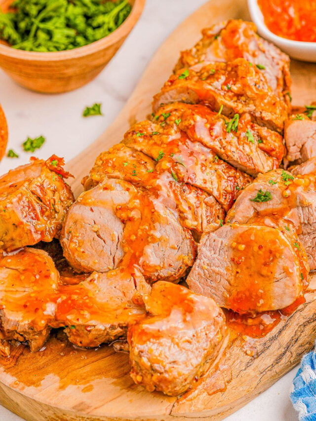 Sliced roasted pork tenderloin with glaze on a wooden cutting board, garnished with parsley.