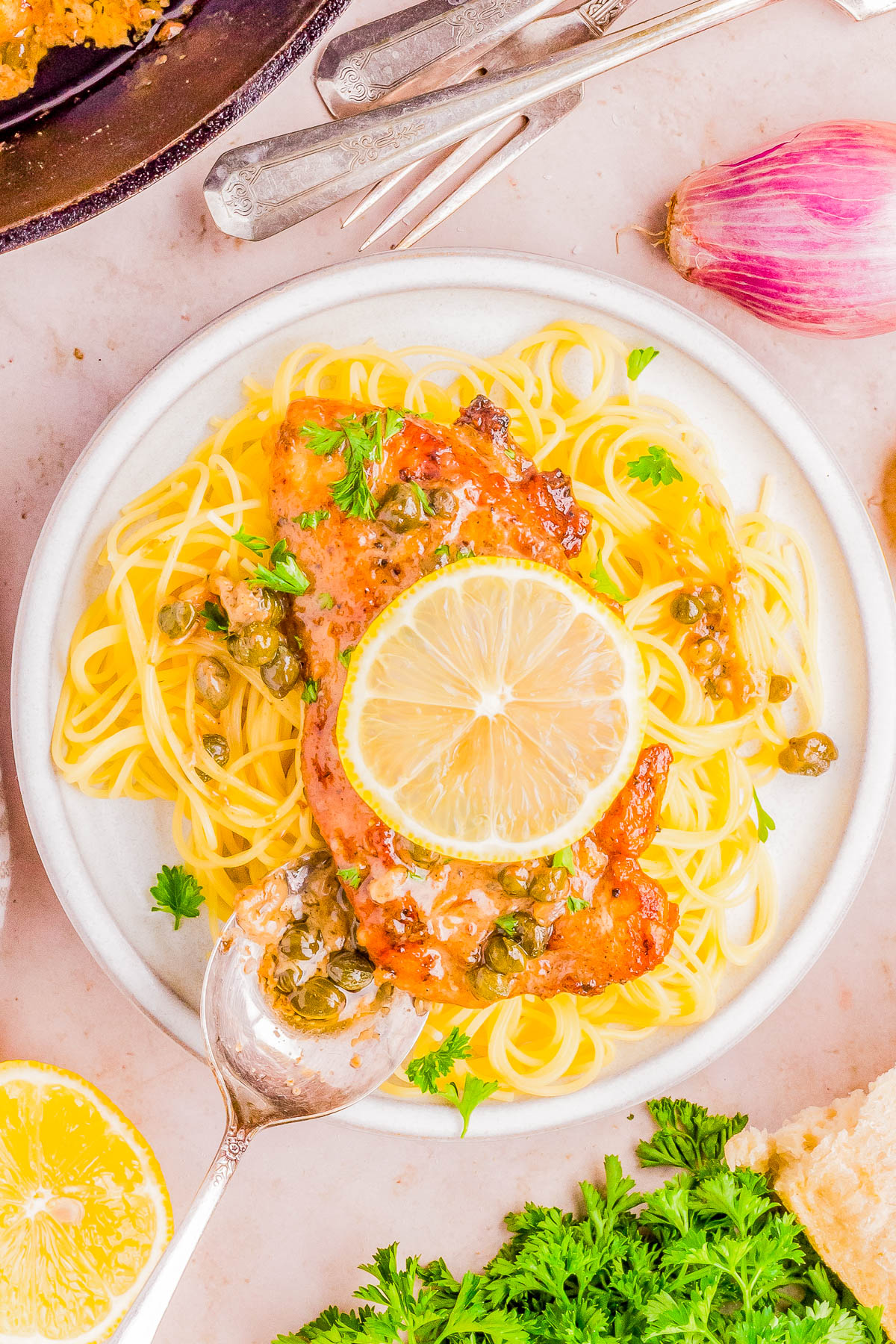 A plate of spaghetti with a lemon-caper sauce and a slice of lemon on top, served with a side of bread and fresh herbs.