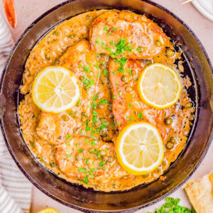 Lemon garlic chicken breasts in a skillet garnished with parsley, alongside ingredients and seasonings.