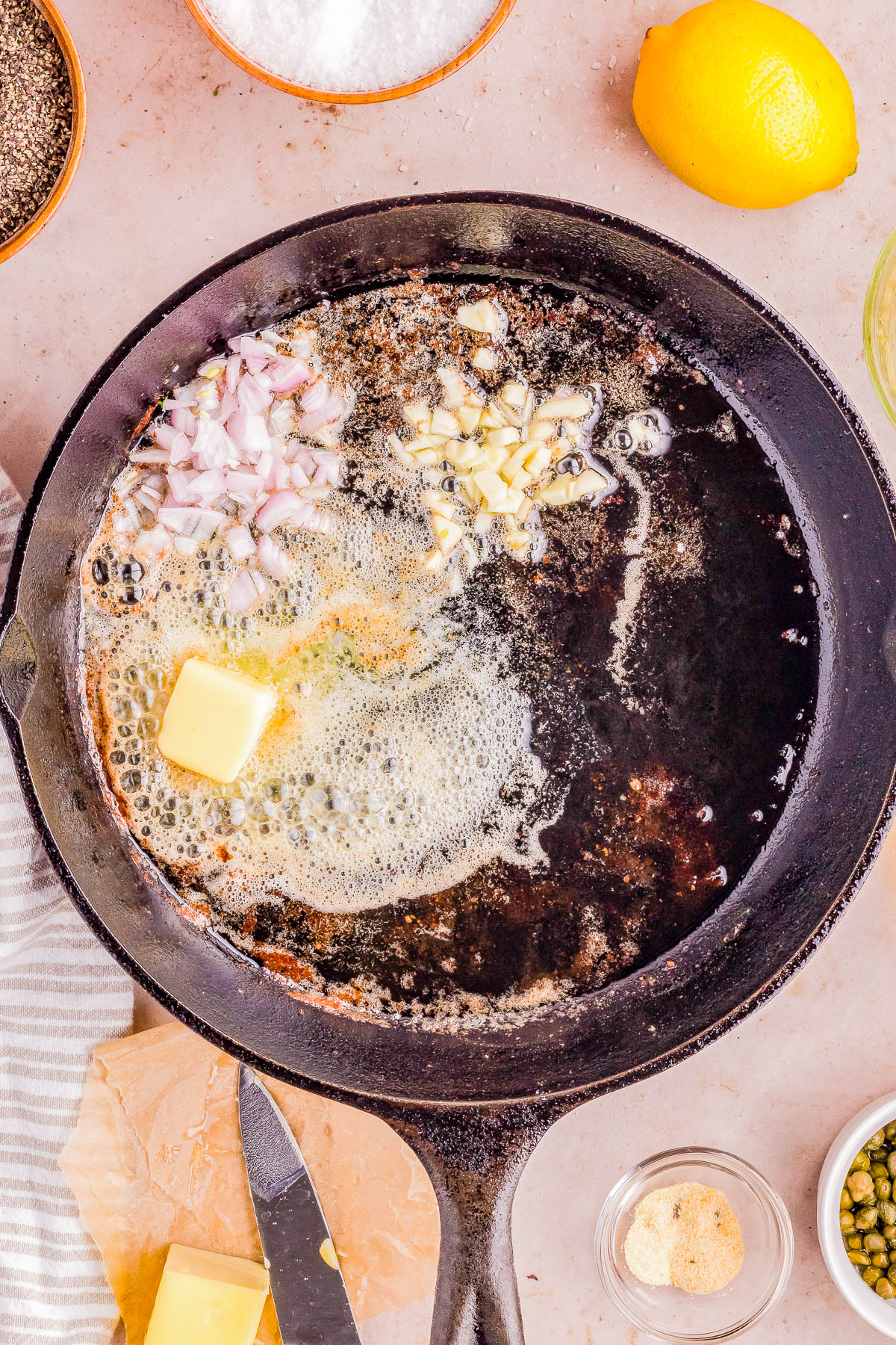 Ingredients being sautéed in butter on a cast-iron skillet, with cooking utensils and spices nearby.