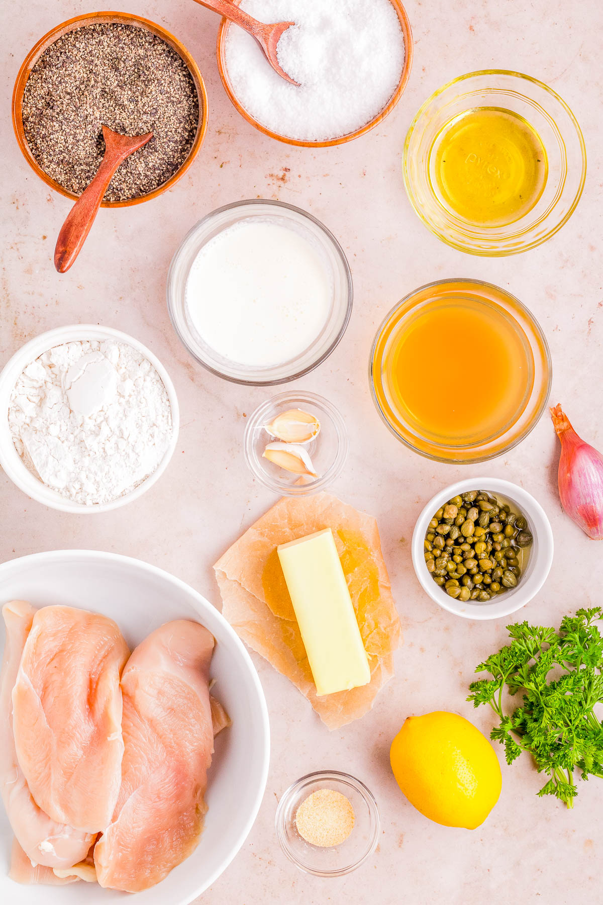 Ingredients for a chicken recipe displayed on a countertop, including raw chicken breasts, lemon, parsley, and various seasonings and oils.
