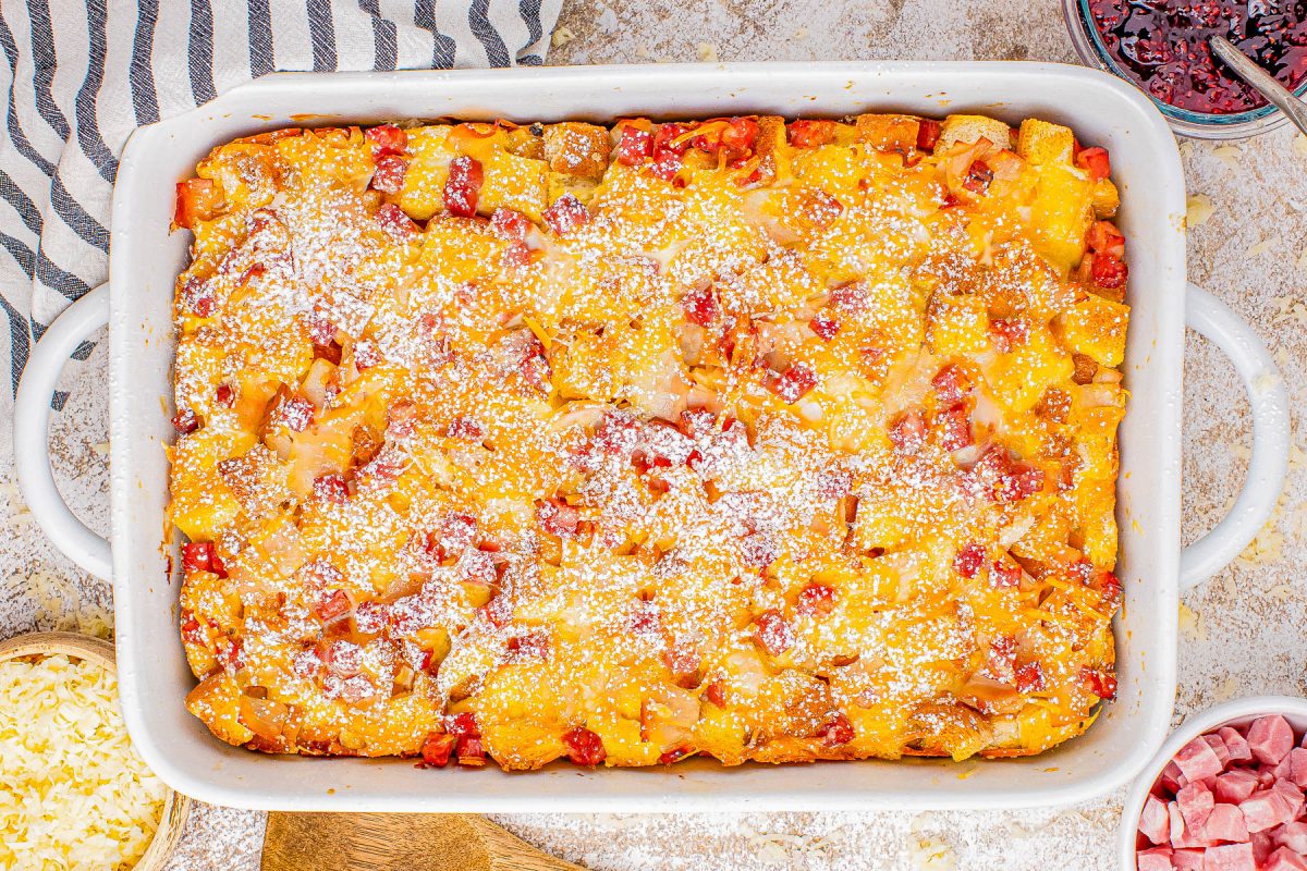 A freshly baked casserole dish with a golden cheesy topping, sprinkled with diced red ingredients and powdered seasoning.