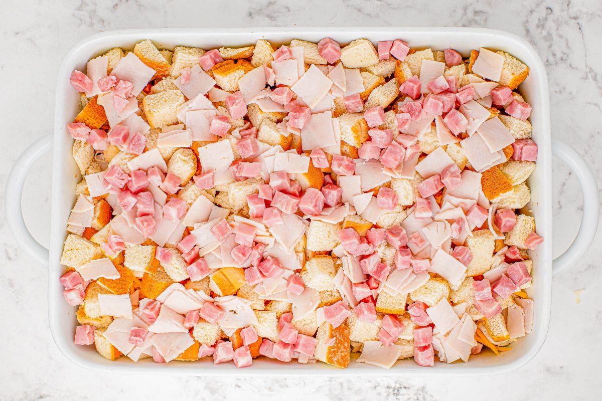 A baking dish filled with cubed bread and chopped ham, prepared for cooking.