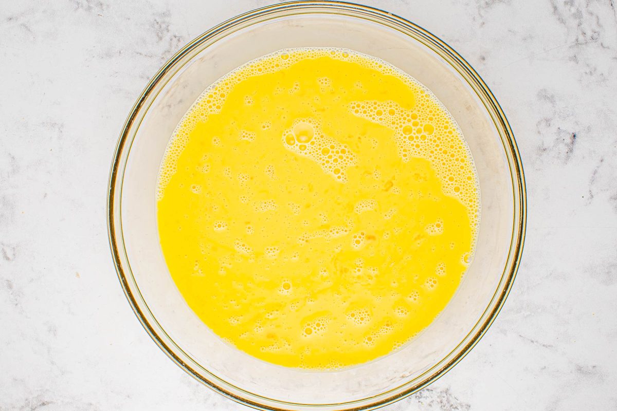 A bowl of whisked eggs with bubbles on a marble surface.