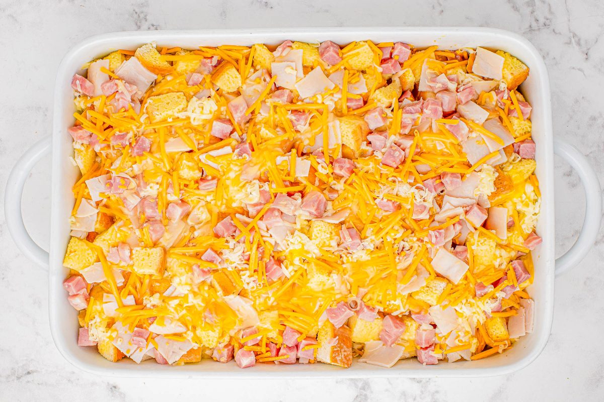 A baking dish filled with nachos topped with cheese and diced ham.