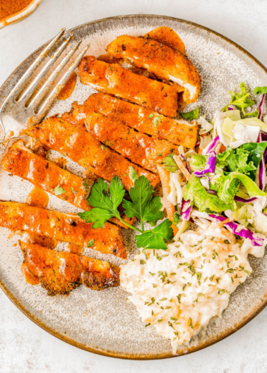 Sliced breaded chicken breast served on a plate with coleslaw and a creamy sauce, garnished with parsley.