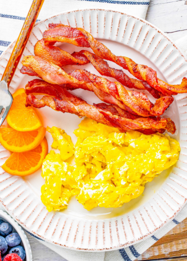 Plate with scrambled eggs, crispy bacon strips, and orange slices.
