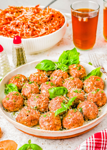A dish of meatballs garnished with basil, served with spaghetti and a glass of iced tea on a table.