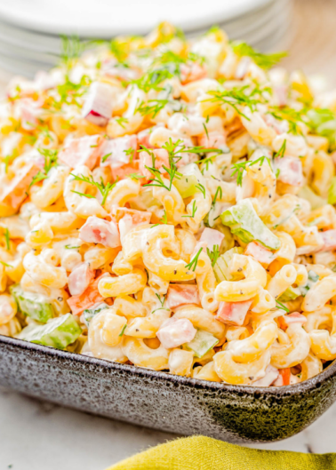 A bowl of creamy macaroni salad with diced vegetables and herbs, served on a yellow napkin.