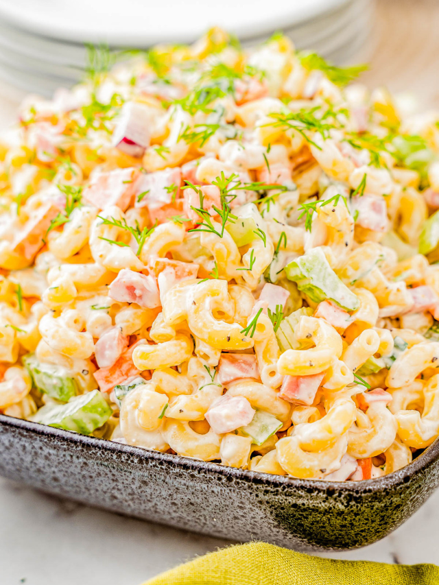 A bowl of creamy macaroni salad with diced vegetables and herbs, served on a yellow napkin.