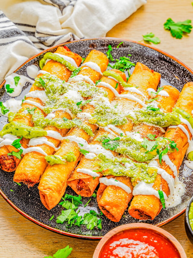 Plate of crispy taquitos drizzled with green sauce and sour cream, garnished with cilantro, served with a side of red salsa.